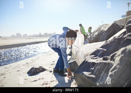 Junge Freiwillige aufnehmen Wurf am sonnigen Strand Stockfoto