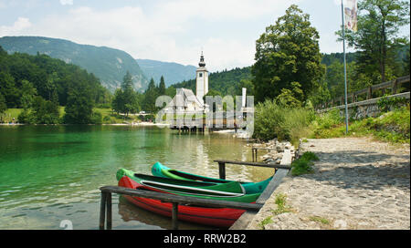 Blick auf die Kirche St. Johannes der Täufer, julischen Alpen und Boote in der Nähe von See, Bohinj, Slowenien Stockfoto