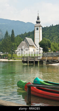 Blick auf die Kirche St. Johannes der Täufer, julischen Alpen und Boote in der Nähe von See, Bohinj, Slowenien Stockfoto