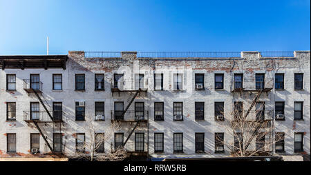 Alte weiße Backsteingebäude mit Windows und Feuerleitern und eine leere und blauer Himmel Overhead in New York City NYC Stockfoto