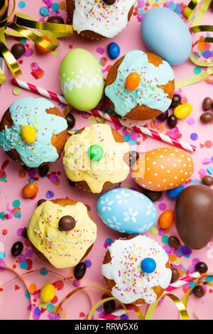 Ostern party Konzept mit Ostern Eier, Muffins, Schokolade, Bonbons, Konfetti, Streamer und Strohhalme auf einem Rosa packground. Ansicht von oben Stockfoto