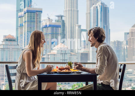 Liebespaar beim Frühstück auf dem Balkon. Frühstück mit Kaffee Obst und Brot, Croissant auf einem Balkon vor dem Hintergrund der großen Stadt Stockfoto