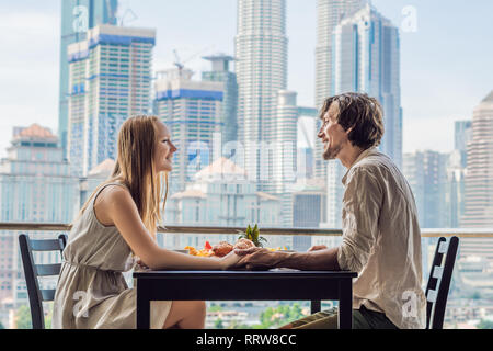 Liebespaar beim Frühstück auf dem Balkon. Frühstück mit Kaffee Obst und Brot, Croissant auf einem Balkon vor dem Hintergrund der großen Stadt Stockfoto