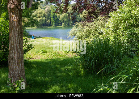 Schönen Parklandschaft. In den Tiefen der Park am Ufer des Sees sehen Sie die Silhouette eines Mannes, der an einem Computer arbeitet (liest, zieht Stockfoto