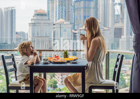 Happy Family Mit Frühstück auf dem Balkon. Frühstück mit Kaffee Obst und Brot, Croissant auf einem Balkon vor dem Hintergrund der großen Stadt Stockfoto