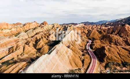 Blick von oben auf die Rainbow Bergen geologischen Park. Stripy Zhangye Danxia Relief geologischen Park in der Provinz Gansu, China. Drone Bild von Touristenbussen Stockfoto