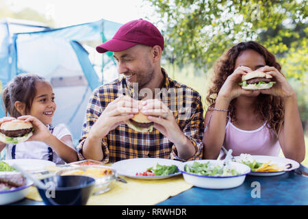 Gerne Vater und Töchter essen Grill Hamburger auf dem Campingplatz Stockfoto