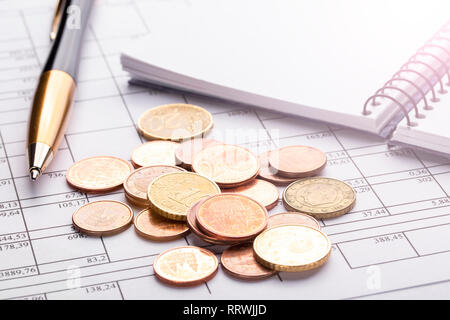 Ein Haufen von Euro-münzen auf einem alten schwarzen Holztisch. Pen, Notebook und Unterlagen. Konzept des Überlebens und Sparmaßnahmen Stockfoto