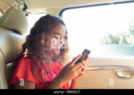 Lächelnd tween Mädchen mit Smart Phone in der Rücksitz des Autos Stockfoto