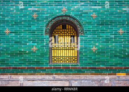 Gelbe Chinesische traditionelle Fenster mit Metallrahmen und Grün Blau Glasierte keramische Fliesen. Tibetische detaillierte Wand. Stockfoto