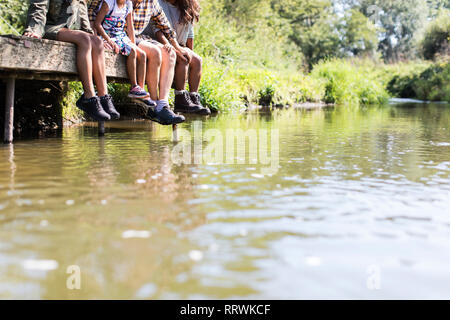 Familie baumelnden Füßen aus sonnigen Riverside dock Stockfoto