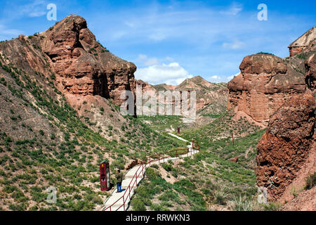 Zu Fuß Mann auf einem Pfad in das Tal, das im Binggou Danxia Canyon Relief in Zhangye, Sunan Region, Provinz Gansu, China. Rote Sandsteinfelsen Stockfoto