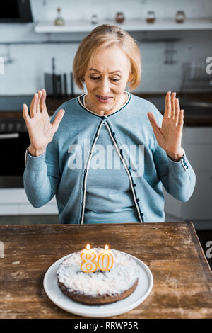 Aufgeregt senior Frau sitzt und Kuchen mit '80' Zeichen auf während der Geburtstagsfeier Stockfoto