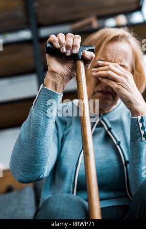 Verärgert ältere Frau mit Spazierstock, das Gesicht mit der Hand und zu Hause weinen Stockfoto