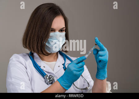 Junge attraktive Krankenschwester mit Maske füllt in der Spritze in der Hand schließen Stockfoto