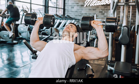 Schöner macht athletischer Mann in Ausbildung Pumpen nach oben Muskeln mit Hanteln in ein Fitnessstudio. - Bild Stockfoto