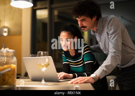 Paar mit Laptop und trinken Wein zu Hause in der Nacht Stockfoto