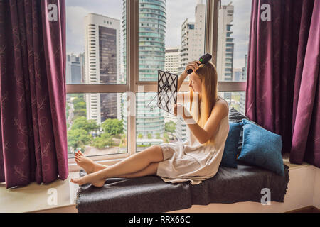 Frau sitzt am Fenster und verwendet ein elektronisches Haarbürste Stockfoto