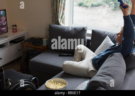 Junge Frau zujubeln, spielen Video Game auf dem Sofa neben Rollstuhl Stockfoto