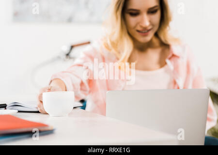 Blonde Frau mit Laptop und Kaffee trinken am Arbeitsplatz Stockfoto