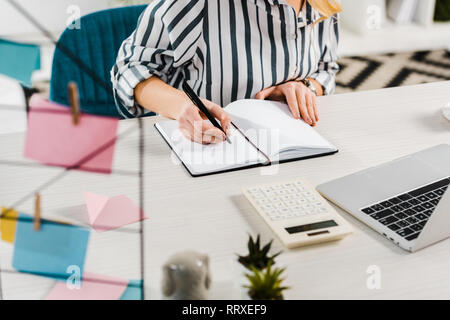 Teilweise mit Blick auf die Frau im gestreiften Hemd schreiben im Notebook am Arbeitsplatz Stockfoto