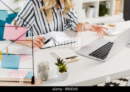 Teilweise mit Blick auf die Frau im gestreiften Hemd holding Kreditkarte und mit Laptop am Arbeitsplatz Stockfoto