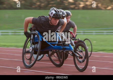 Entschlossene junge weibliche paraplegic Athlet Beschleunigung zusammen Sport Track im Rollstuhl Rennen Stockfoto