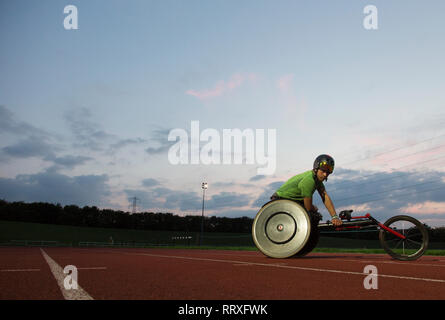 Jungen männlichen querschnittsgelähmten Athlet Training für Rollstuhl Rennen am Sportplatz in der Nacht Stockfoto