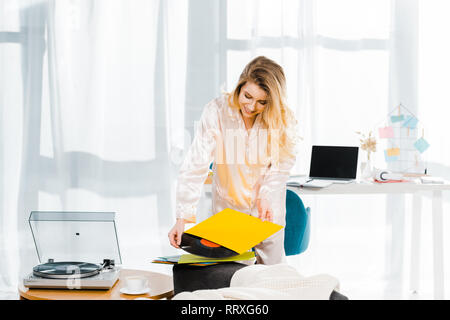 Lächelnde Frau in Satin Schlafanzug holding Schallplatte in Morgen Stockfoto