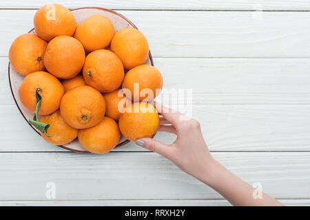 Teilweise mit Blick auf die weibliche Hand in der Nähe der Platte mit Mandarinen auf hölzernen weißen Hintergrund Stockfoto