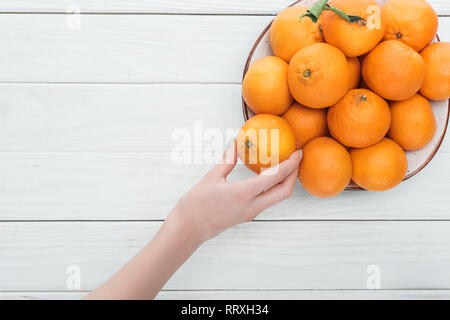 Teilweise mit Blick auf die weibliche Hand in der Nähe der Platte mit Mandarinen auf hölzernen weißen Hintergrund mit Kopie Raum Stockfoto