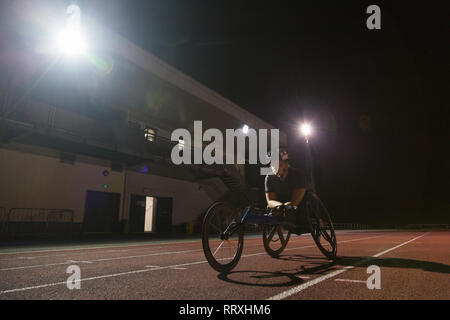 Bestimmt weiblichen paraplegic Athlet Training für Rollstuhl Rennen am Sportplatz in der Nacht Stockfoto