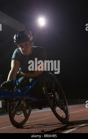 Portrait entschlossene junge weibliche paraplegic Athlet Training für Rollstuhl Rennen am Sportplatz in der Nacht Stockfoto