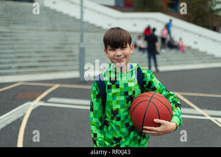 Portrait zuversichtlich tween Junge mit Basketball in Schulhof Stockfoto