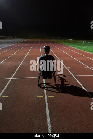 Entschlossene junge weibliche paraplegic Athlet Training für Rollstuhl Rennen am Sportplatz in der Nacht Stockfoto