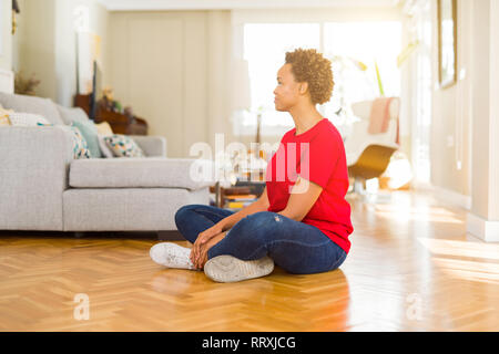 Junge schöne afrikanische amerikanische Frau auf dem Boden zu Hause sitzen, entspannen Sie sich auf der Seite Profil mit natürliches Gesicht mit selbstbewussten Lächeln darstellen. Stockfoto
