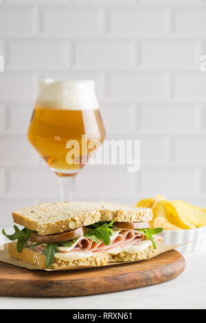 Lecker Sandwich mit Schinken, Käse, Salat und Tomaten mit einem Glas Bier und Chips auf hellen Hintergrund Stockfoto