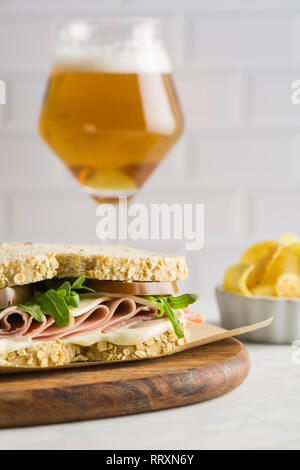 Lecker Sandwich mit Schinken, Käse, Salat und Tomaten mit einem Glas Bier und Chips auf hellen Hintergrund Stockfoto