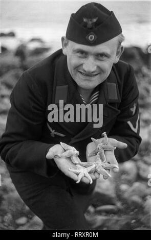 Frankreich - Frankreich in den 1940er Jahren. Le Havre - Deutsche Marine sailor mit Seestern am Strand. Foto von Erich Andres Essenrode, Mann mit Seesternen am Strand von Le Havre, 1940er Jahre. Stockfoto