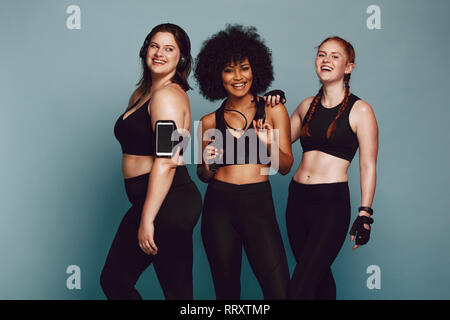 Portrait von gemischten Rennen Frauen gemeinsam gegen das grauen Hintergrund stehen und Lachen. Vielfältige Gruppe Frauen in Sportbekleidung. Stockfoto