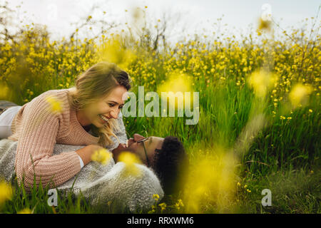 Wunderschöne liegende Frau mit ihrem Freund auf dem hohen Gras und lächelnd. Junge Paare, die auf dem Gras in jeder anderen suchen und lächelnd. Stockfoto