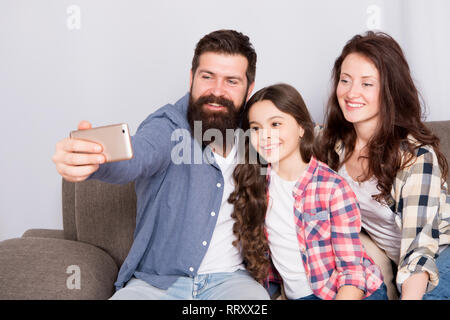 Familie verbringen Wochenende zusammen. Verwendung des Smartphones für selfie. Freundliche Familie gemeinsam Spaß zu haben. Mama, Papa und Tochter entspannt auf einer Couch. Familie posieren für Fotos. Glückliche Momente festzuhalten. Familie selfie. Stockfoto