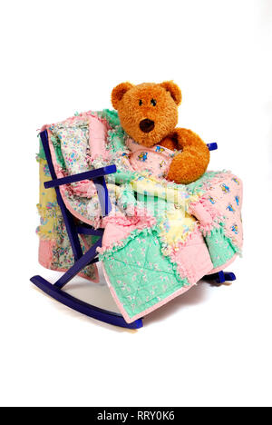 Ein Teddybär sitzt auf einem vintage Kind Schaukelstuhl mit einem Rag quilt getröstet. Stockfoto