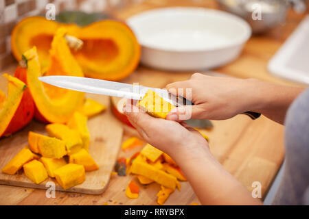 Frau schneiden Sie den Kürbis mit einem Messer in Ihrer Küche Stockfoto