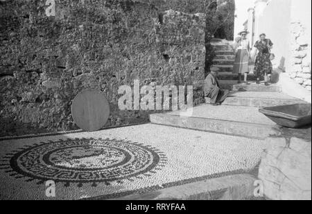 Spanien, Griechenland - Ein Mann und zwei Touristinnen in einer Gasse von Lindos auf Rhodos, Griechenland, 1950er Jahre. Ein Mann und zwei Touristen auf einer Fahrspur in Lindos auf der Insel Rhodos, Griechenland, 1950. Stockfoto