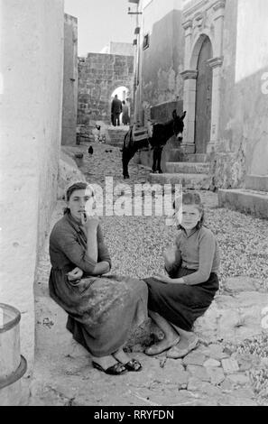 Spanien, Griechenland - Zwei junge Frauen Artikel vor dem Haus auf der Straße bei einer Unterhaltung in Rhodos, Griechenland, 1950er Jahre. Zwei junge Frauen, die vor dem Haus sitzen, während sie in Rhodos, Griechenland, 1950. Stockfoto