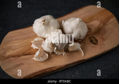 Drei Köpfe von Knoblauch (Allium sativum) auf einem Schneidebrett aus Olivenholz. Stockfoto