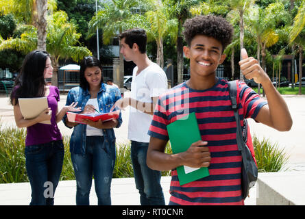 Afrikanische männliche Kursteilnehmer mit Daumen mit einer Gruppe von anderen internationalen Studenten auf dem Campus der unniversity im Freien Stockfoto