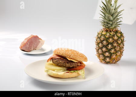 Cheeseburger mit Ananas auf eine Platte auf einen weißen Hintergrund mit frischen Speck und reife Ananas Stockfoto