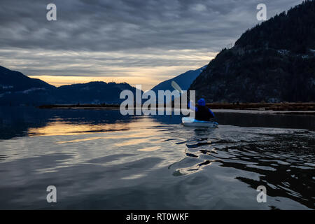 Abenteuerliche mann Kajak im ruhigen Wasser während eine trübe winter Sonnenuntergang. In Squamish, nördlich von Vancouver, BC, Kanada. Stockfoto